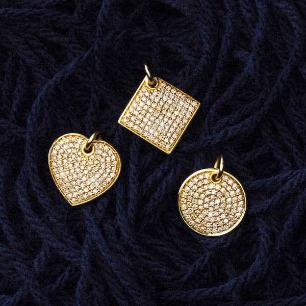3 champagne diamond yellow gold name pendants styled together atop a heap of dark blue yarn. The heart, diamond and round shapes.